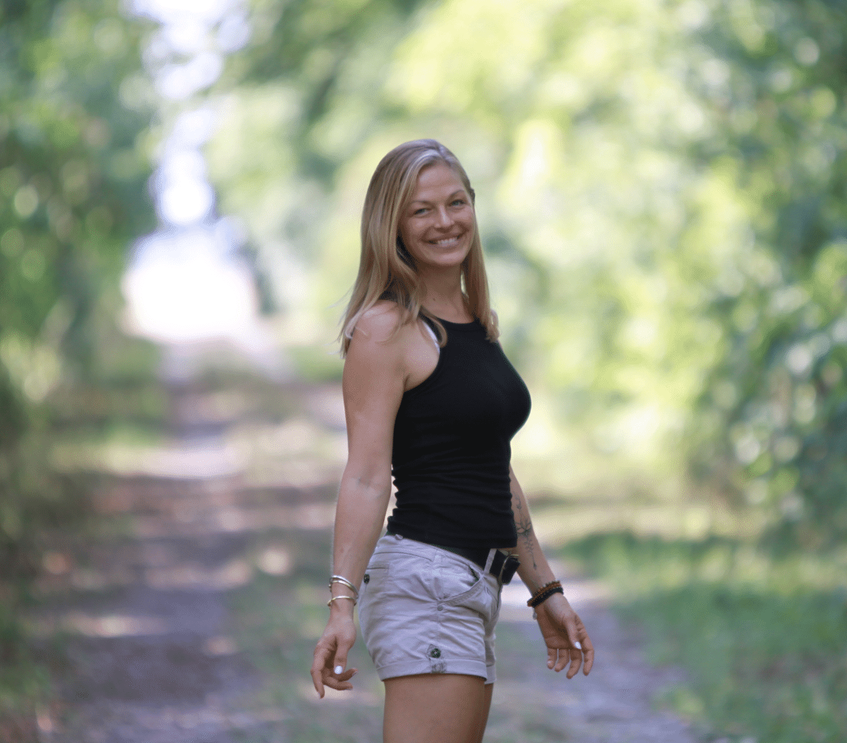 Blonde-woman-with-open-hair-on-forest-path-turns-around-and-looks-back-with-an-inviting-smile