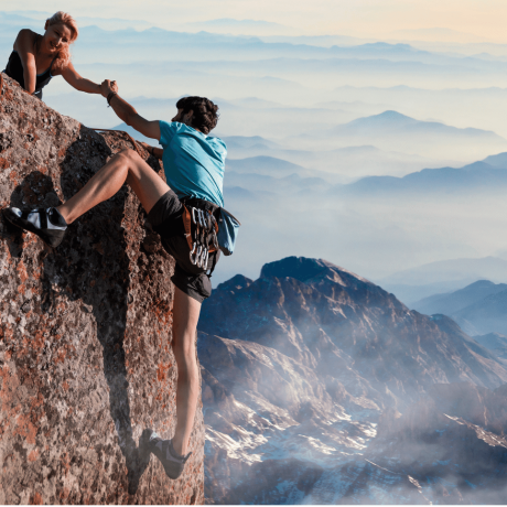Was meine Arbeit ausmacht_Loyalität_Frau zieht Mann über Klippenrand auf Berspitze hoch Teamwork-woman-helps-man-climb-over-a-cliff-in-beautiful-mountains-by-shaking-his-hand-from-above
